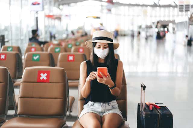 Una mujer con mascarilla en un aeropuerto junto a asientos anulados por la pandemia.