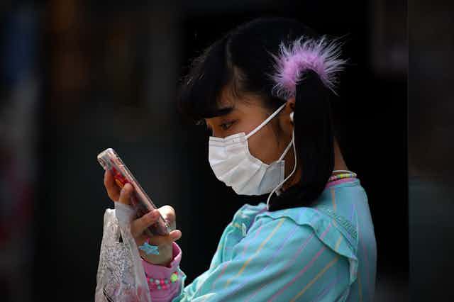 Girl wearing face mask holds mobile phone close to face