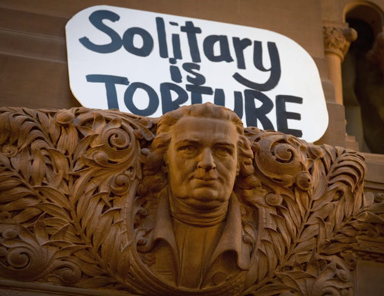 Protest sign saying 'solitary is torture' displayed at the New York State Assembly's Great Western Staircase