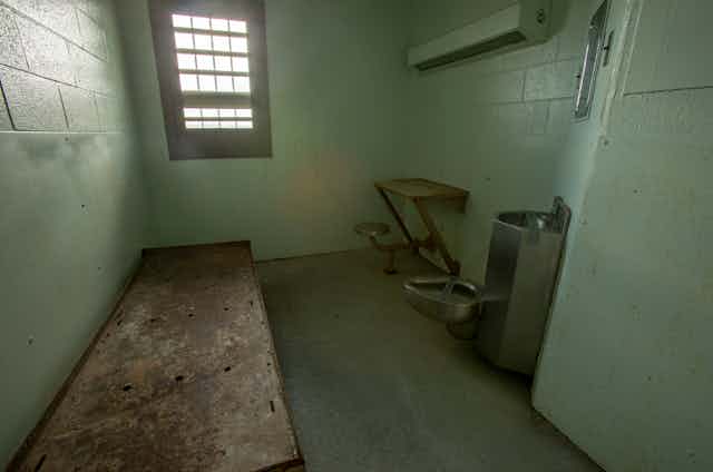 Interior of solitary confinement cell with metal bed, desk and toilet in an old prison