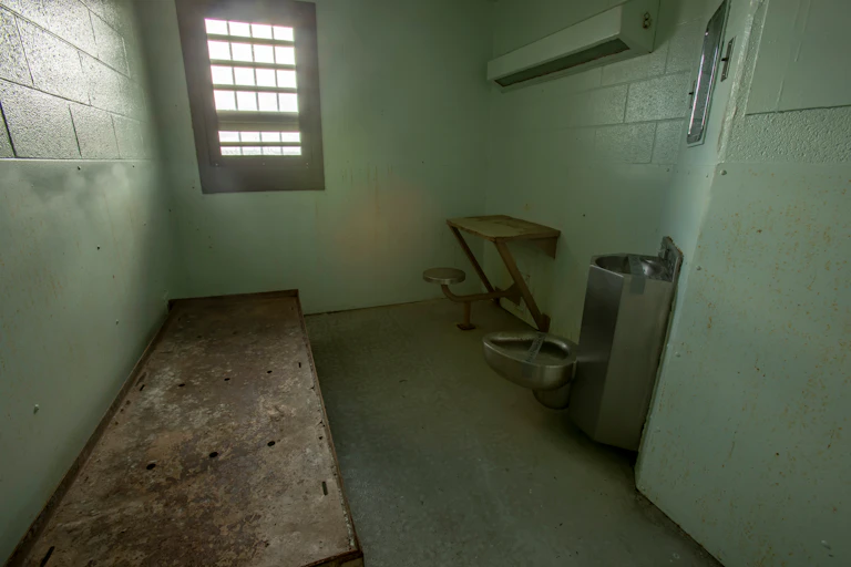 Interior of solitary confinement cell with metal bed, desk and toilet in an old prison