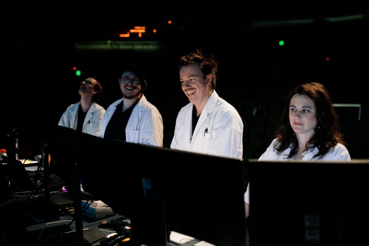 Four cast members smile  at computers