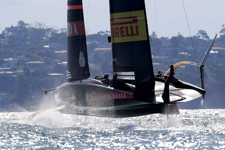 America's Cup yacht foiling with land and houses in background