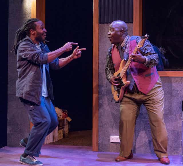 Two Black men dance, one plays a guitar