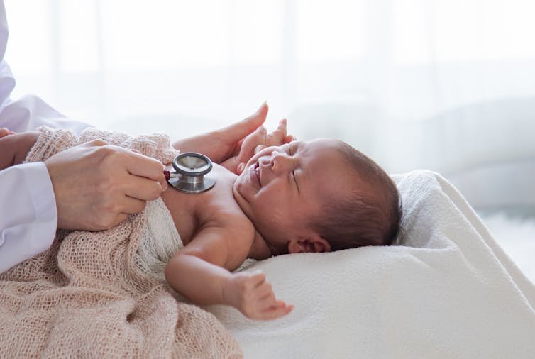 A doctor holds a stethoscope to a baby's chest.