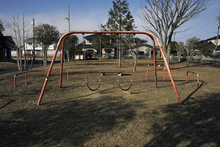 A red swing set stands alone in a vacant neighbourhood park.