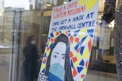 A woman walks near a sign offering face masks