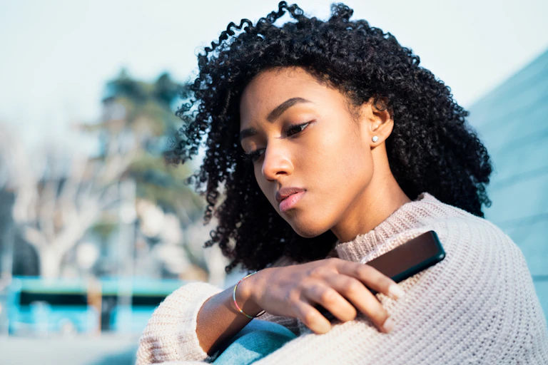 A Black woman holds her mobile phone outside.