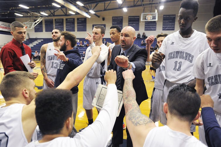 Basketball players huddle together with their coach.