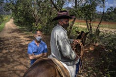 A man in a mask sits on a horse while another man stands behind him, also wearing a mask.