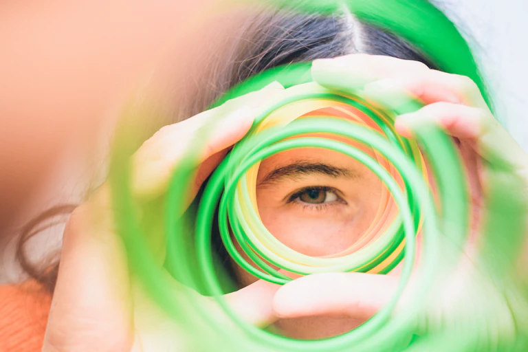 A young woman's eye seen through her hands holding a colored spiral