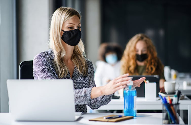 Office workers wearing masks, one santising hands
