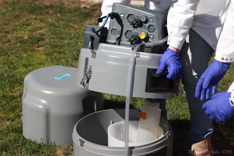 Gloved researchers open an autosampler to remove a bottle of liquid.