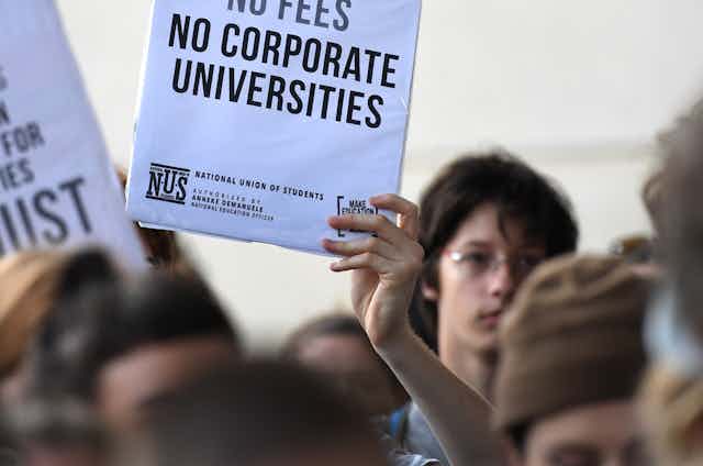 Student holding sign 'NO CORPORATE UNIVERSITIES' at protest