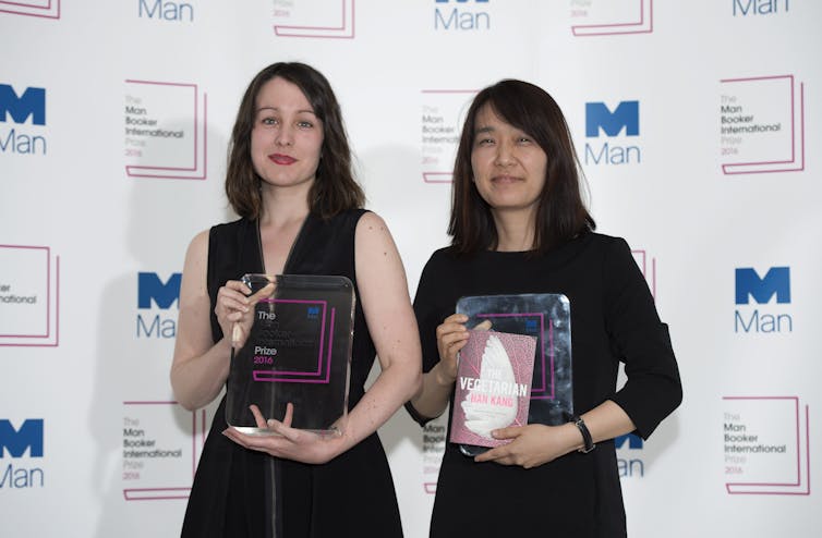 A white woman and an Asian woman pose with trophies.