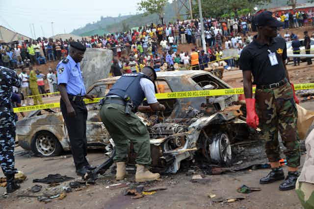 Men in police and military uniforms inspecting car wreckage left on the street following a bomb blast