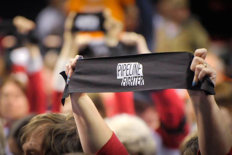 A person in a large crowd holds an armband aloft reading 'Pipeline Fighter'