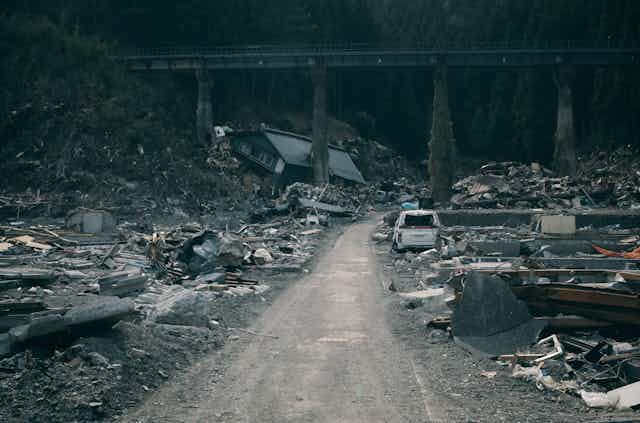 A road with cars and rubble on either side, a bridge in the background.