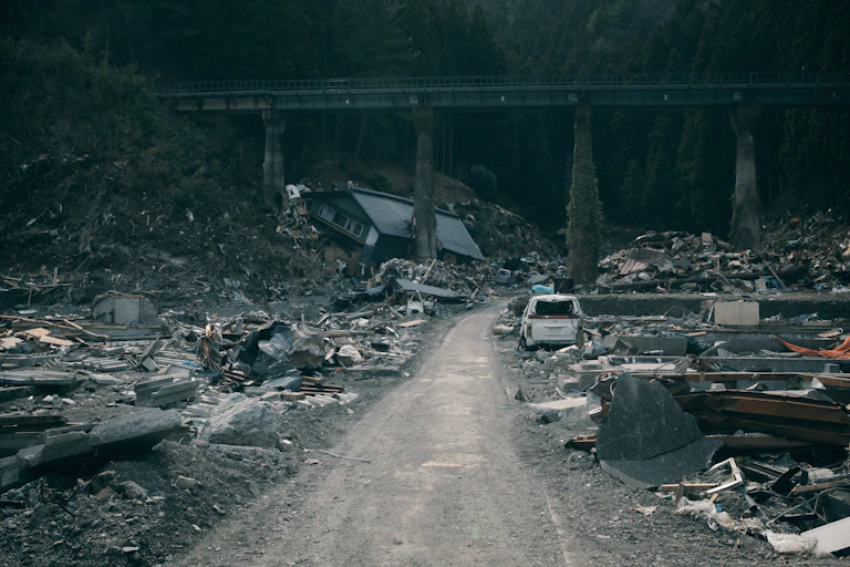A road with cars and rubble on either side, a bridge in the background.
