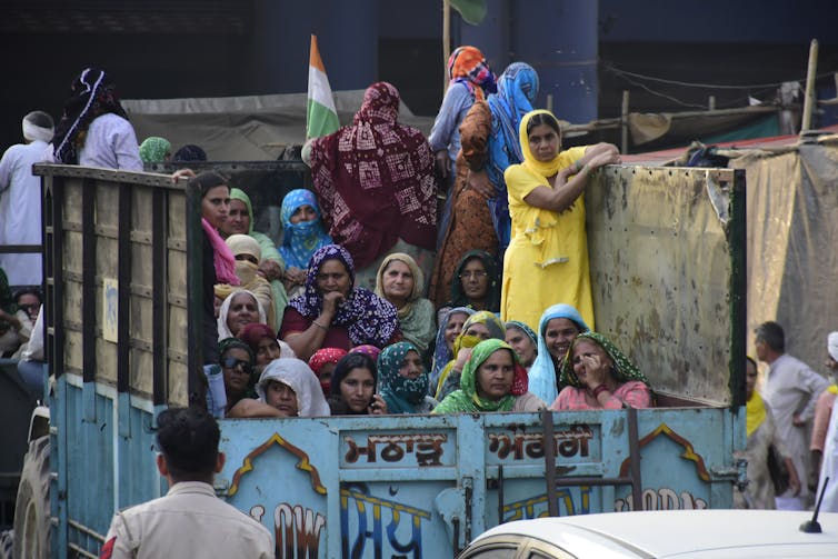 Dozens of Indian women look solemnly defiant riding in the back of a truck