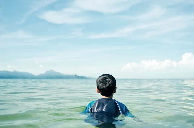 Rear view of a boy sitting in the ocean.