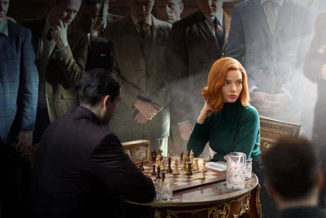 A woman playing chess surrounded by men.