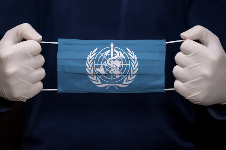 Person with gloves on holding face mask with WHO logo on.