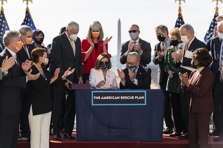 Senate Majority Leader Chuck Schumer claps as House Speaker Nancy Pelosi signs the $1.9 trillion COVID-19 relief bill, as other Democrats look on.