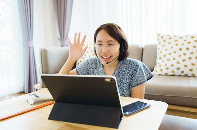 Mature student waves as she talks online using a laptop