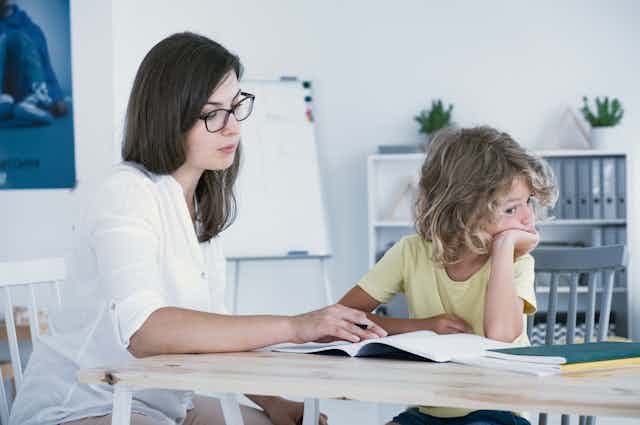 Woman helps child with learning as child looks away