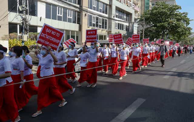 Nurses, all in red skirts, white tops and face masks, hold up signs saying 'Say No to Dictatorship. Free Our Leaders'