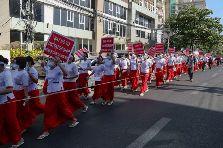 Nurses, all in red skirts, white tops and face masks, hold up signs saying 'Say No to Dictatorship. Free Our Leaders'