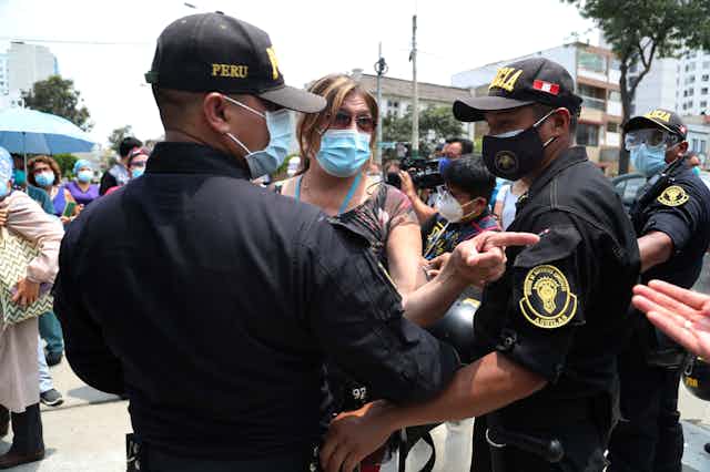 A woman in a mask is stopped by two police officers wearing masks.