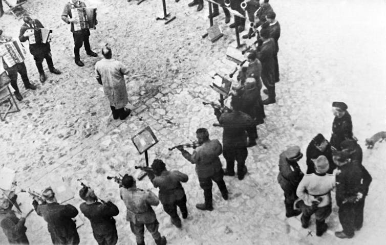 Performers form a circle around a man as guards observe.