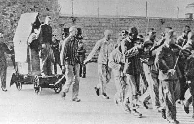 A group of prisoners march and play instruments as they lead a boy to execution.