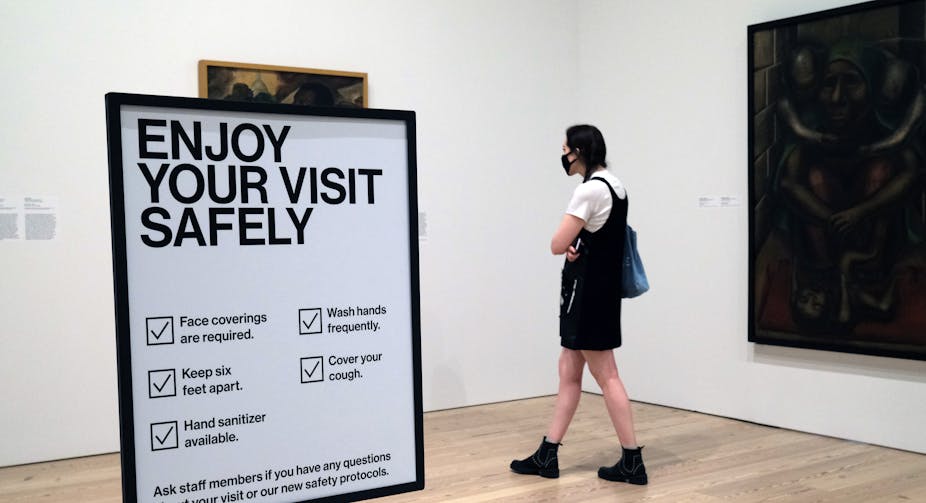 A woman looks at a painting amid health and safety warnings.