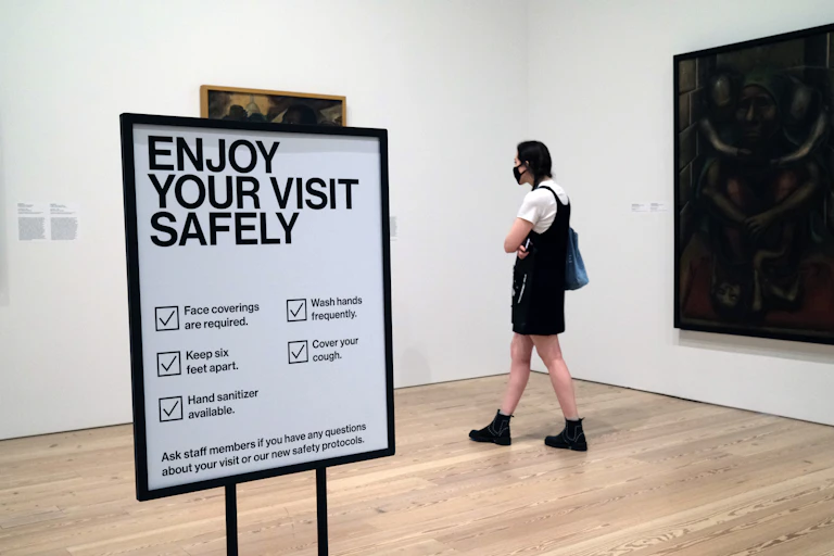 A woman looks at a painting amid health and safety warnings.