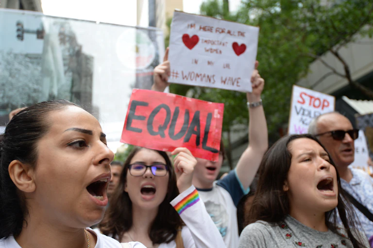 Women at protest march holding signs and yelling.