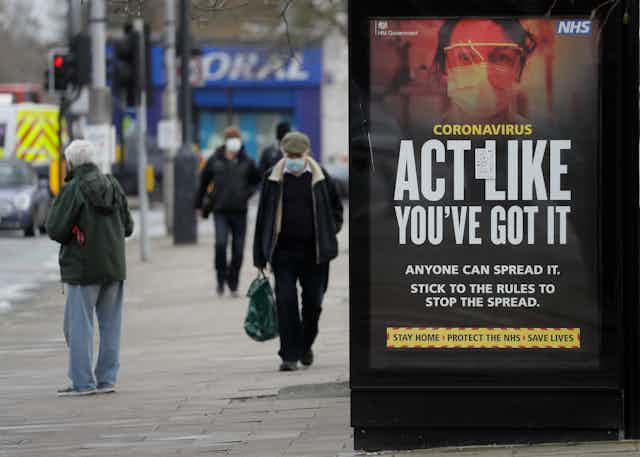 People walking wearing masks in London, next to a sign saying 'act like you've got it'.