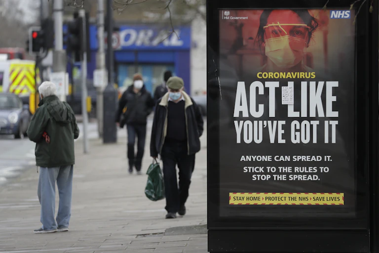 People walking wearing masks in London, next to a sign saying 'act like you've got it'.