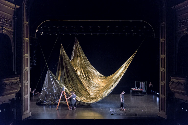 A vast stage. A gold curtain. Two women.
