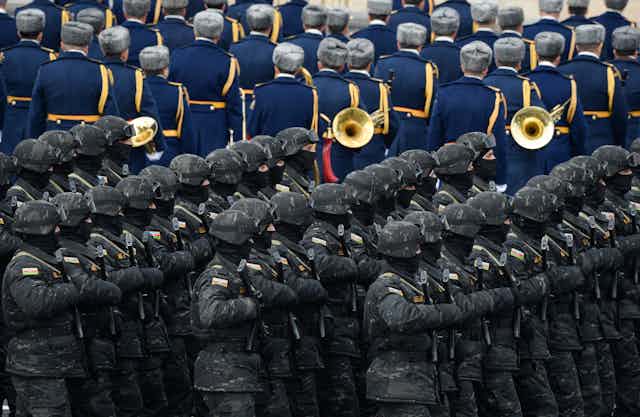 Troops march beside a military band.