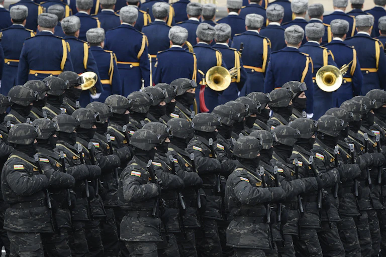 Troops march beside a military band.
