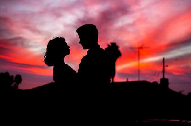 young couple embrace with sunset behind