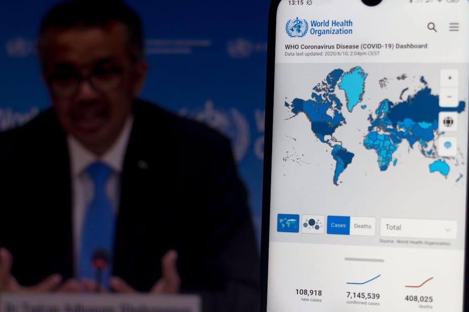 WHO director general Tedros Adhanom Ghebreyesus is seen on a screen of pc with a WHO coronavirus cases map displayed on a smartphone
