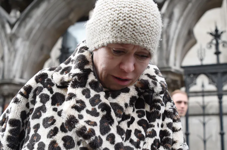 A woman in a beanie hat and a faux leopard-skin coat looking upset as she leaves the High Court in London.