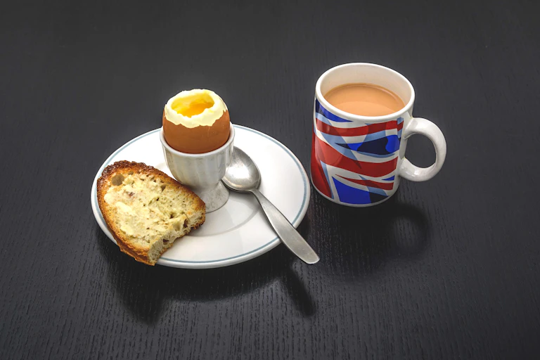 Boiled egg and toast on a plate next to a Union Jack mug filled with tea