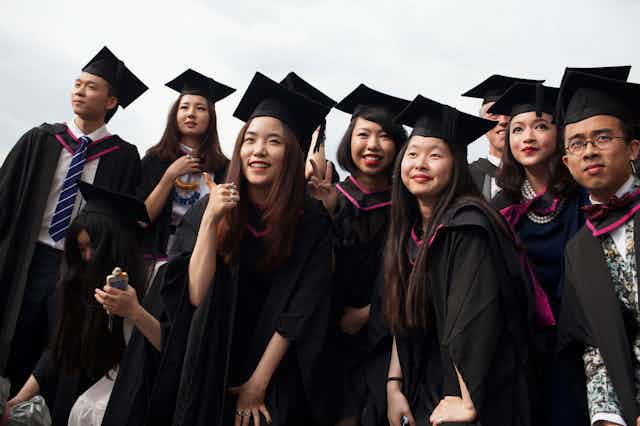 A group of young Chinese graduates in academic caps and gowns after graduating from the UNiversity of the Arts in London.