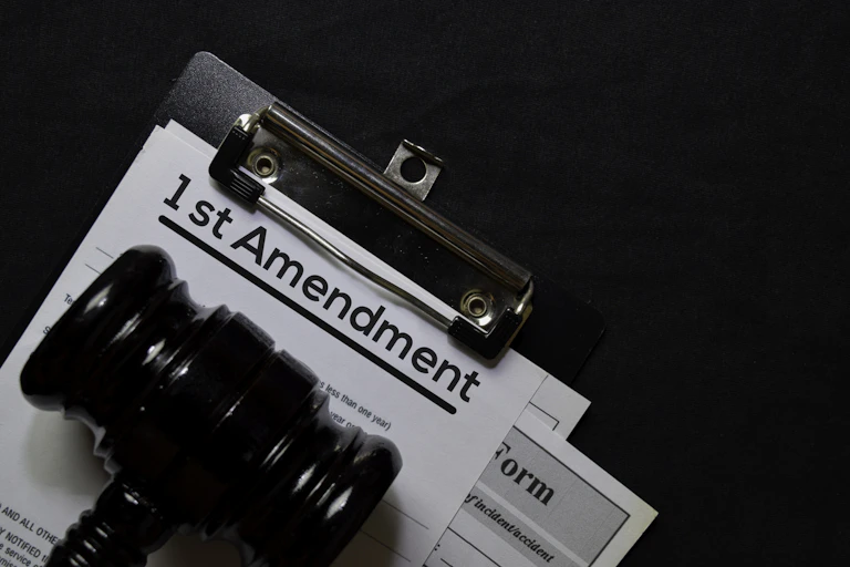 A clipboard with a page that says "1st Amendment" on it, under a judge's gavel