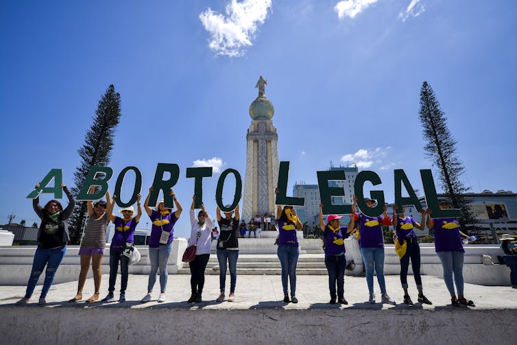 Women stand in a row in a plaza holding letters that spell out 'aborto legal'